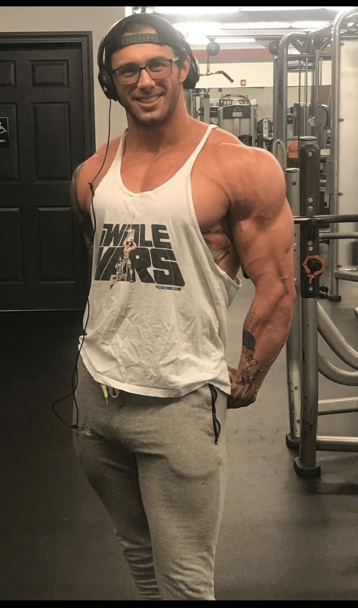 Jed Hannaford smiling in the gym, wearing headphones and a white tank top